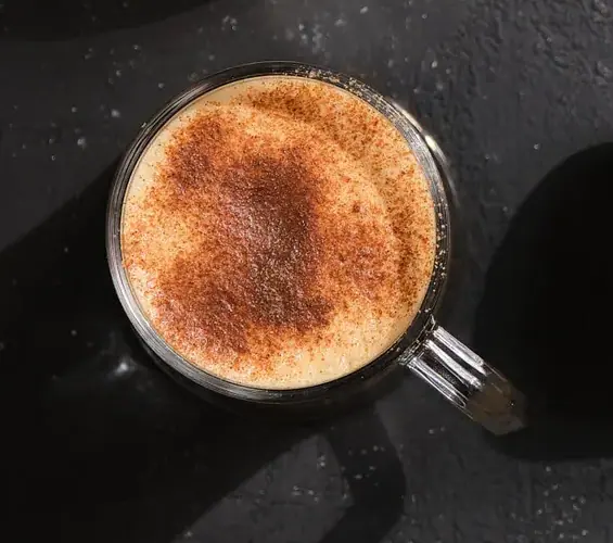 Foamy pumpkin-spice coffee in a clear glass mug