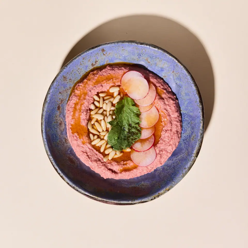 Pink beet and galangal hummus topped with radish slices, seeds, and herbs