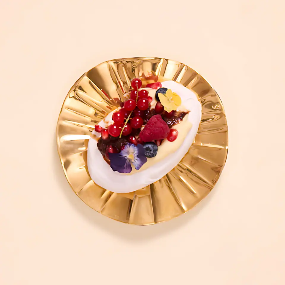 Berry pavlova with cream, blueberries, and red berries on a gold plate