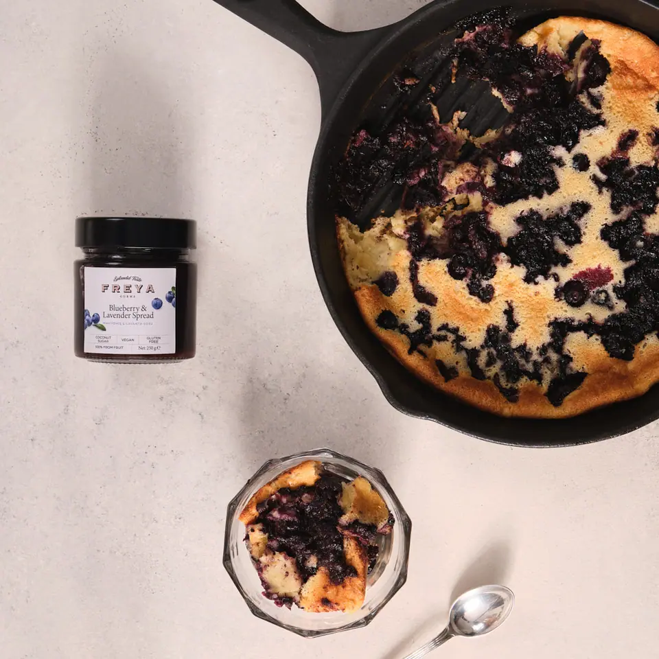 Blueberry lavender clafoutis in a round baking pan with a serving in a small bowl