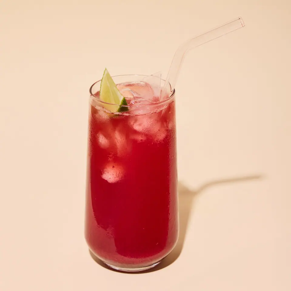 Cherry and rhubarb gin and tonic with ice and lime in a tall glass