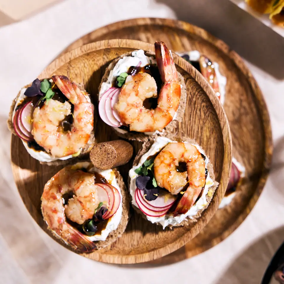 Shrimp canapés with red onion and herbs on a wooden serving board