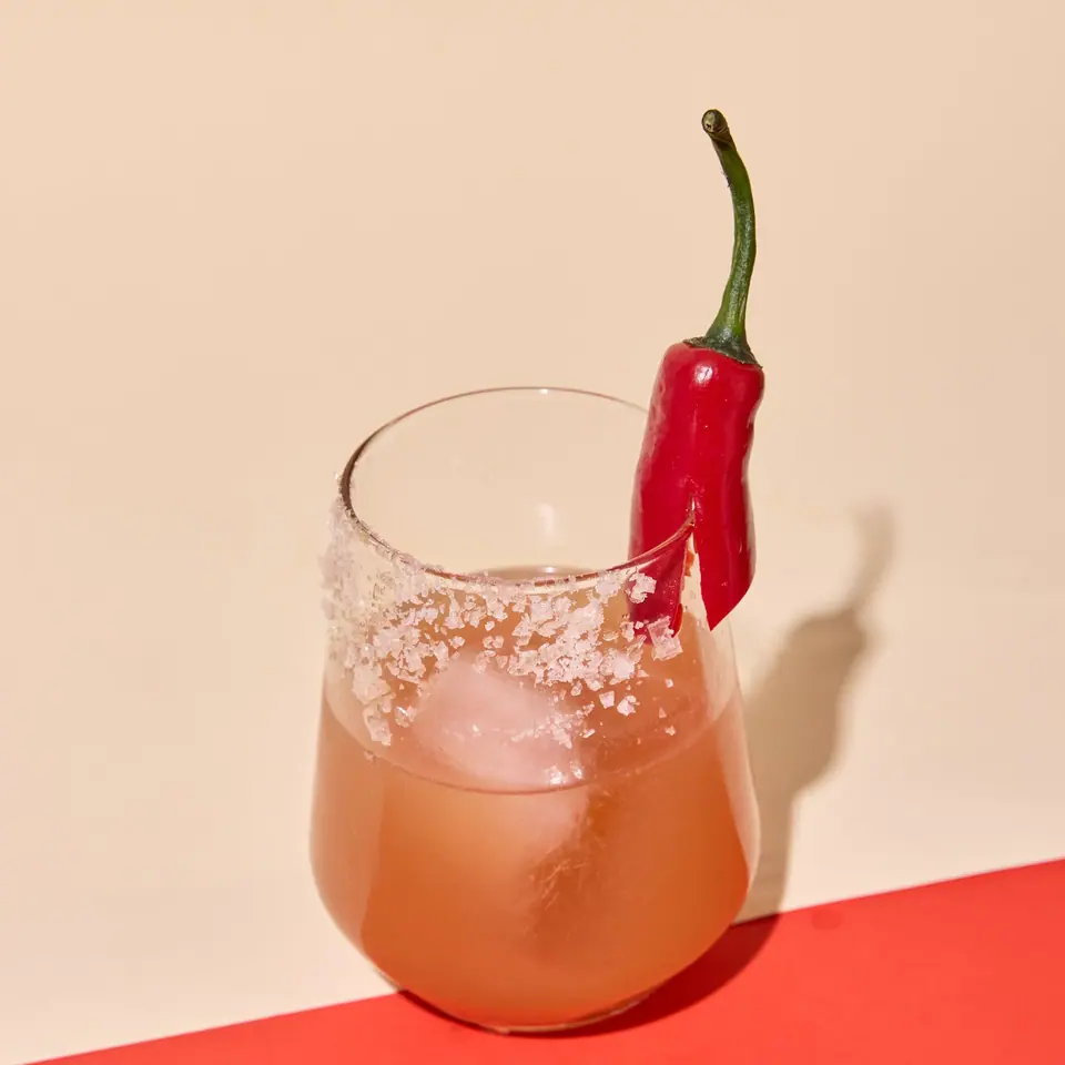 Strawberry jalapeño mezcal cocktail with ice, a salted rim, and a red chili garnish